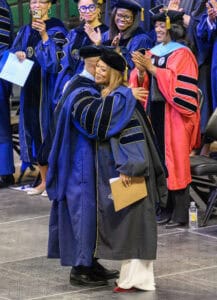 Graduates in academic regalia celebrating at graduation ceremony on stage.