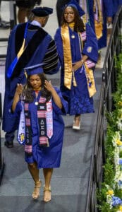 Graduates in blue caps and gowns celebrating at graduation ceremony with honor cords and medals.