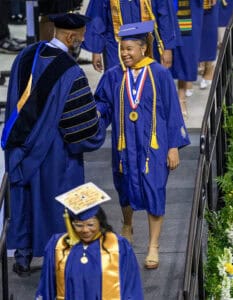 Graduation ceremony with smiling graduates in blue caps and gowns, celebrating academic achievement.