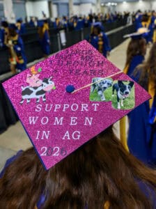 Support women in agriculture graduation cap with cow and dog images at a ceremony.