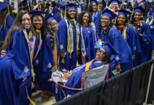 Graduates in blue caps and gowns celebrating at a graduation ceremony.