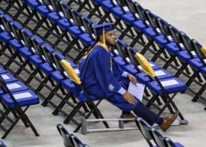 Graduation graduate sitting alone in empty auditorium with blue chairs and diploma.
