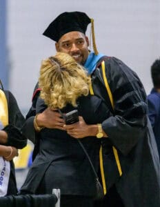 Graduation celebration with smiling graduate hugging a woman in academic gown and cap.