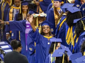 Graduates in blue caps and gowns celebrating at a graduation ceremony.