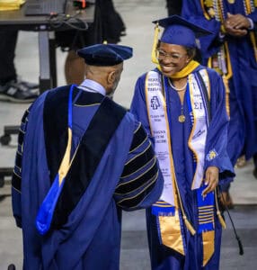 Graduation ceremony with smiling graduate in blue cap and gown receiving diploma at CAES News event.