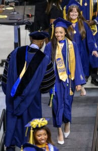 Graduates in blue caps and gowns celebrating at graduation ceremony.