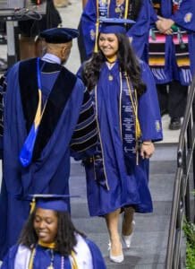 Graduation ceremony with smiling graduate in blue cap and gown at CAES News event.