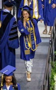 Graduation cap and gown ceremony with smiling graduate in blue attire celebrating achievement.