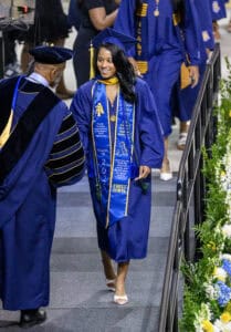 Graduation cap and gown ceremony with smiling graduate receiving diploma at commencement event.