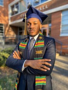 Graduation graduate in cap and gown outside university building, celebrating academic achievement.