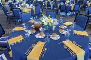 Elegant banquet table set with yellow napkins, glassware, bread rolls, and a floral centerpiece at a.